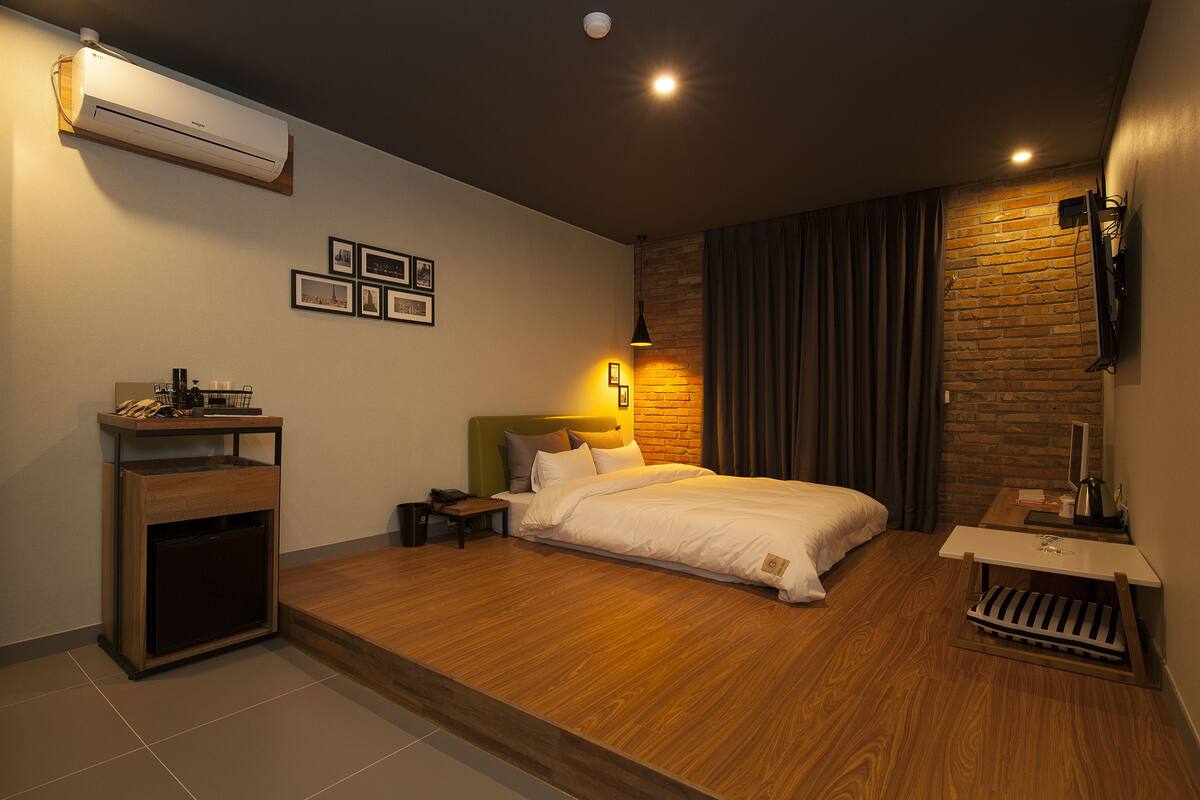 A modern hotel room with a bed, bedside table, lamp, and an air conditioning unit.