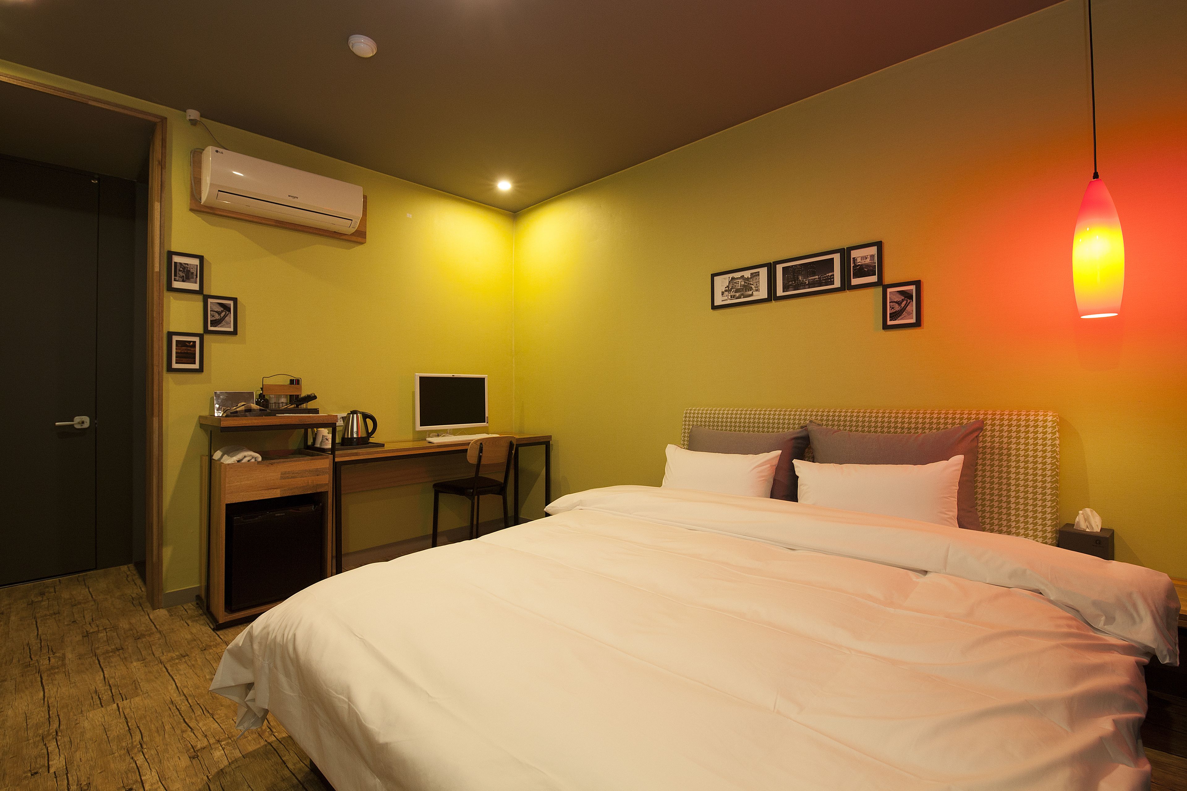 A hotel room with a bed, desk, chair, and an air conditioning unit.