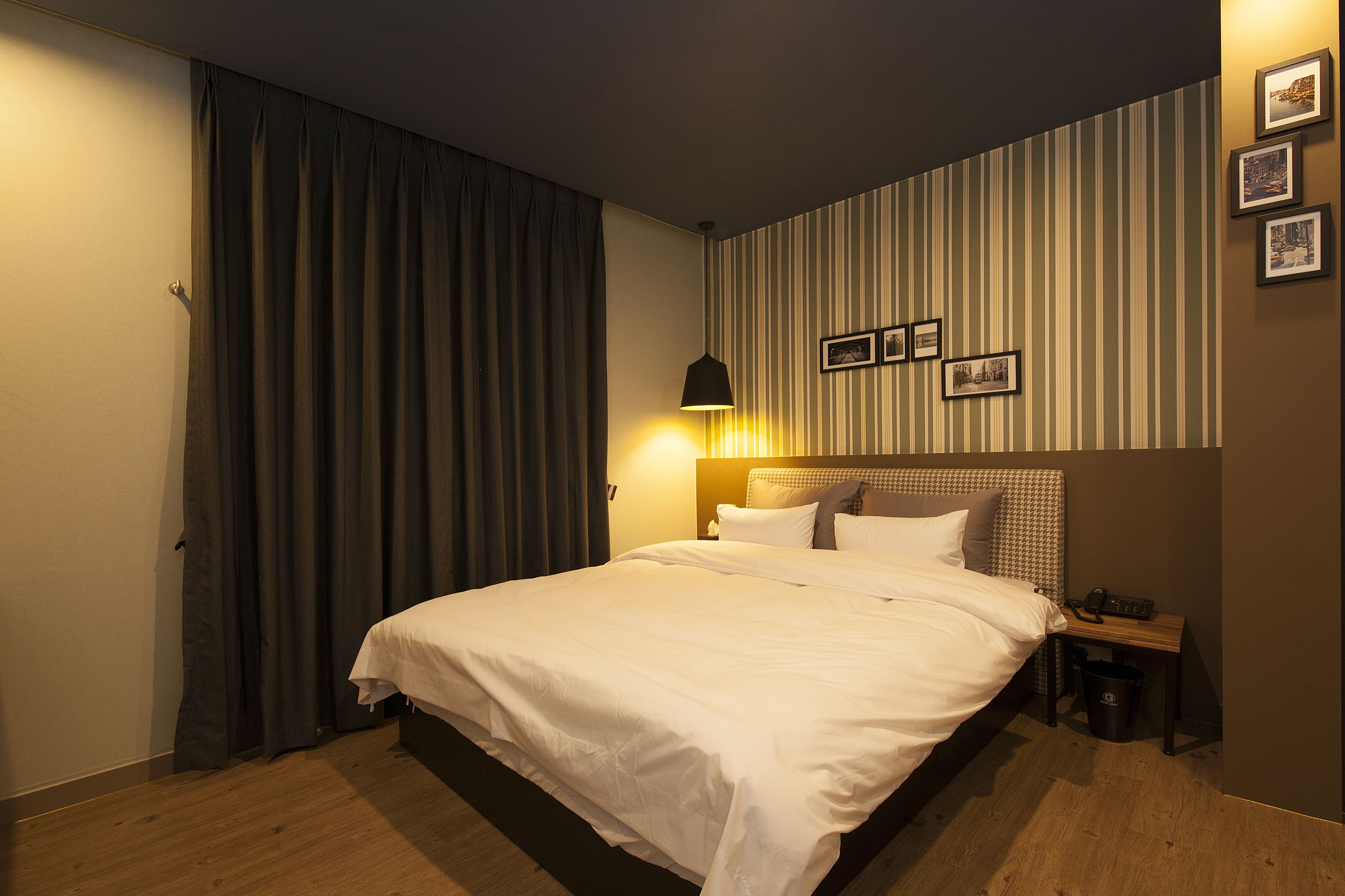 A hotel room with a large bed, a bedside table, a lamp, and a wall with striped wallpaper and framed pictures.