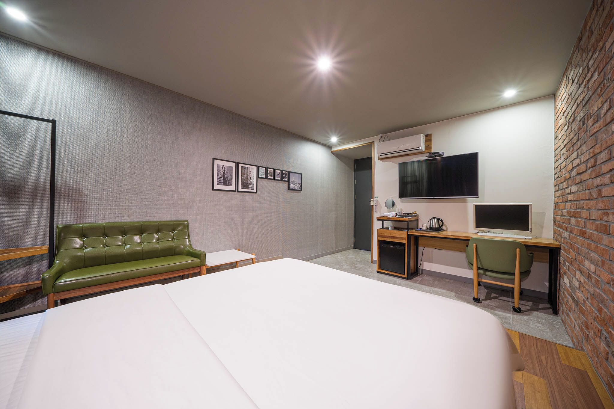 Habitación de hotel con una cama grande, un sofá verde, un escritorio con computadora, televisor y aire acondicionado instalado en la pared.