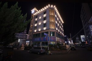 Un hotel de varios pisos con señalización iluminada, entrada visible y zona de estacionamiento.