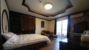 A bedroom with a large bed, a wooden floor, a ceiling light, a TV, and a window with a view. - Bali Motel (Gongju)