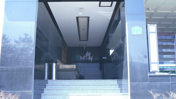 A building entrance with a glass door, a set of stairs leading up, and a sign with the number 32-23. - Bali Motel (Gongju)