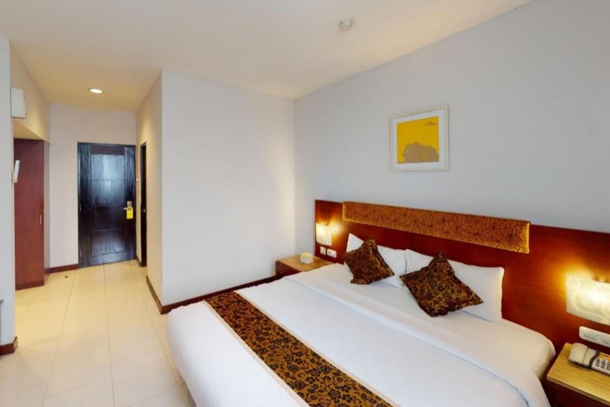 Ein Hotelzimmer mit einem großen Bett, Nachttischen, einem Schreibtisch, einer Tür und einer wandmontierten Lampe.