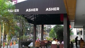 Un espace extérieur aménagé avec des sièges, doté d’un auvent portant l’inscription « ASHER » et d’une plante en pot.