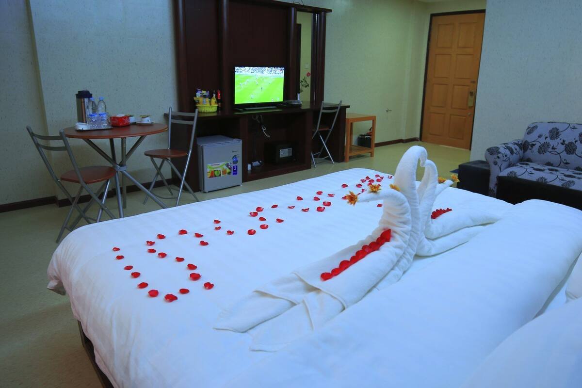 Quarto de hotel com uma cama bem arrumada, televisão, sofá e escrivaninha com um computador.