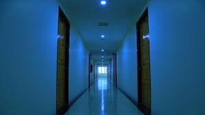 Un pasillo largo y estrecho con puertas de madera a ambos lados, que conduce a un extremo luminoso.