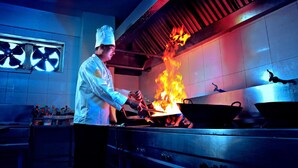 Un chef cocina con llamas en una cocina profesional.