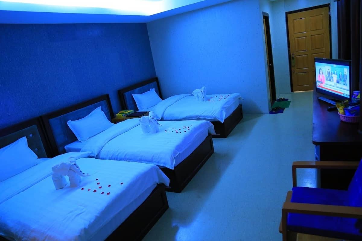 Quarto de hotel com três camas, cada uma com roupa de cama e toalhas brancas, e uma televisão sobre uma mesa.