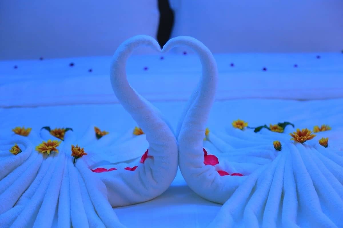 Uma cama com um arranjo em formato de coração feito de toalhas brancas e flores.