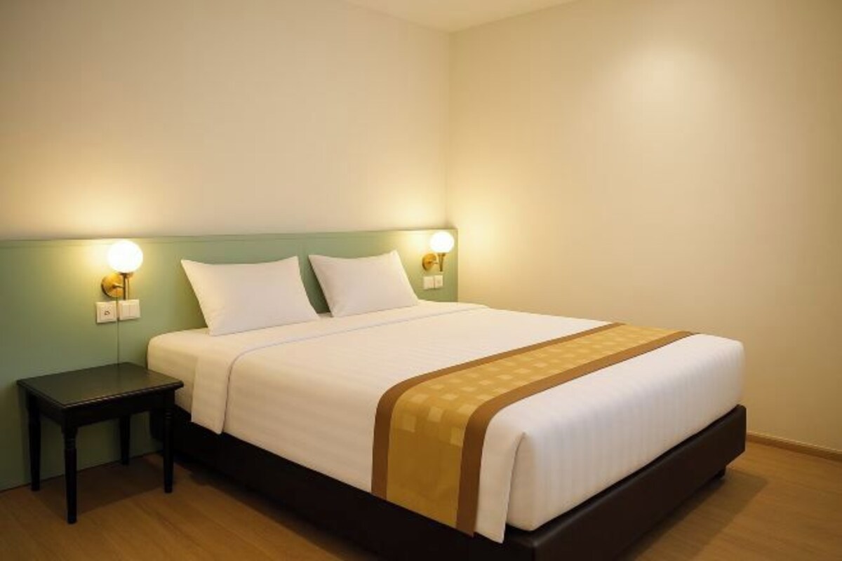 Una cama bien hecha con sábanas blancas y un detalle en marrón, flanqueada por dos mesitas de noche con lámparas, en una habitación con paredes lisas y suelo de madera.