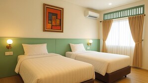 Habitación de hotel con dos camas, un cabecero verde, un cuadro, un equipo de aire acondicionado y una ventana con cortinas.