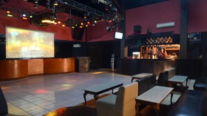 Zona de bar con mostrador, asientos y una pantalla de proyección mostrando texto.