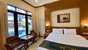 Habitación de hotel con cama, escritorio, dos sillas, ventana con vista a una piscina y dos lámparas de pared.