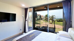 Habitación de hotel con una cama grande, un televisor de pantalla plana montado en la pared y un balcón con suelo a cuadros y mobiliario exterior.