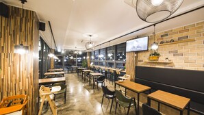 Un interior de restaurante moderno con detalles de madera, sillas negras y de madera, y un televisor montado en la pared.