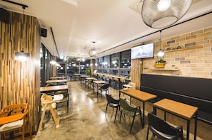 Enjoy meals in a stylish dining area with wooden tables, a cushioned bench, and a mounted TV for entertainment.