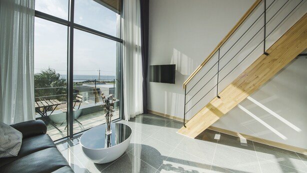 Una sala de estar moderna con un ventanal grande, un sofá, una mesa de centro y una escalera de madera.