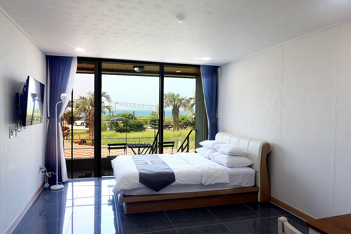 A bedroom with a bed, a TV, and a view of the outdoors.