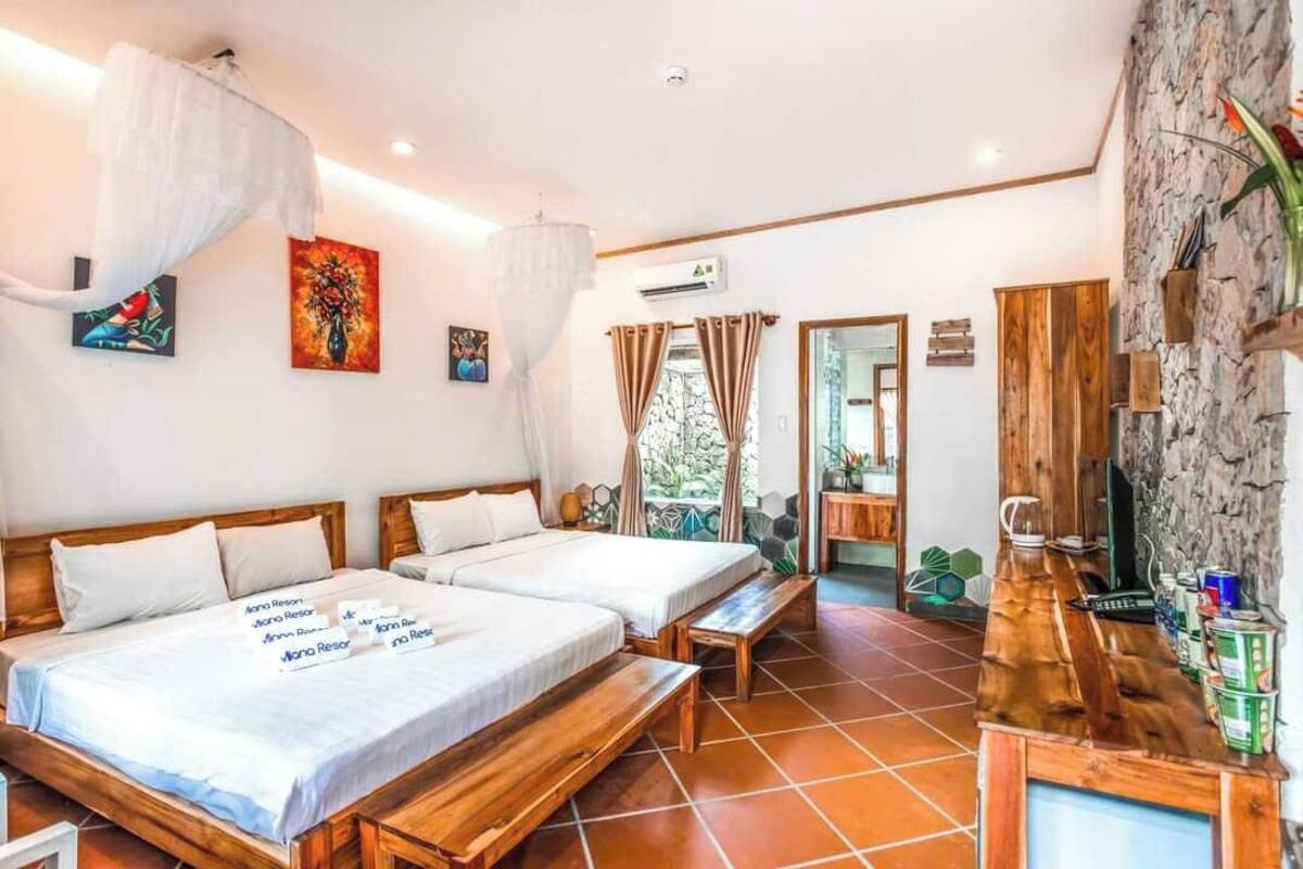 A hotel room with two beds, a wooden desk, and a stone wall.