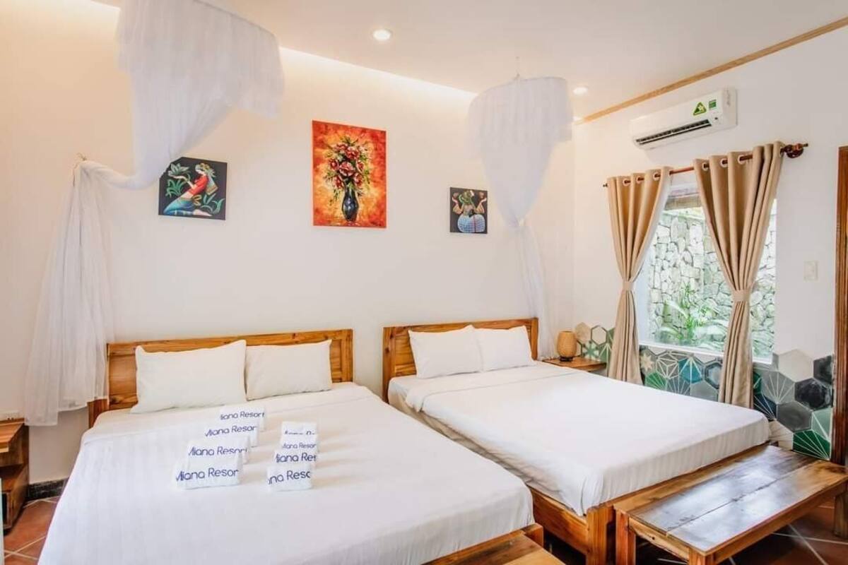 A hotel room with two single beds, a wooden bench, a nightstand, and artwork on the walls.