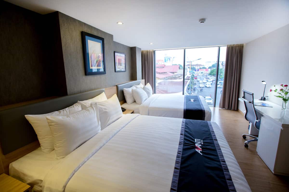 Ein Hotelzimmer mit zwei Betten, einem Schreibtisch und Blick auf die Stadt.