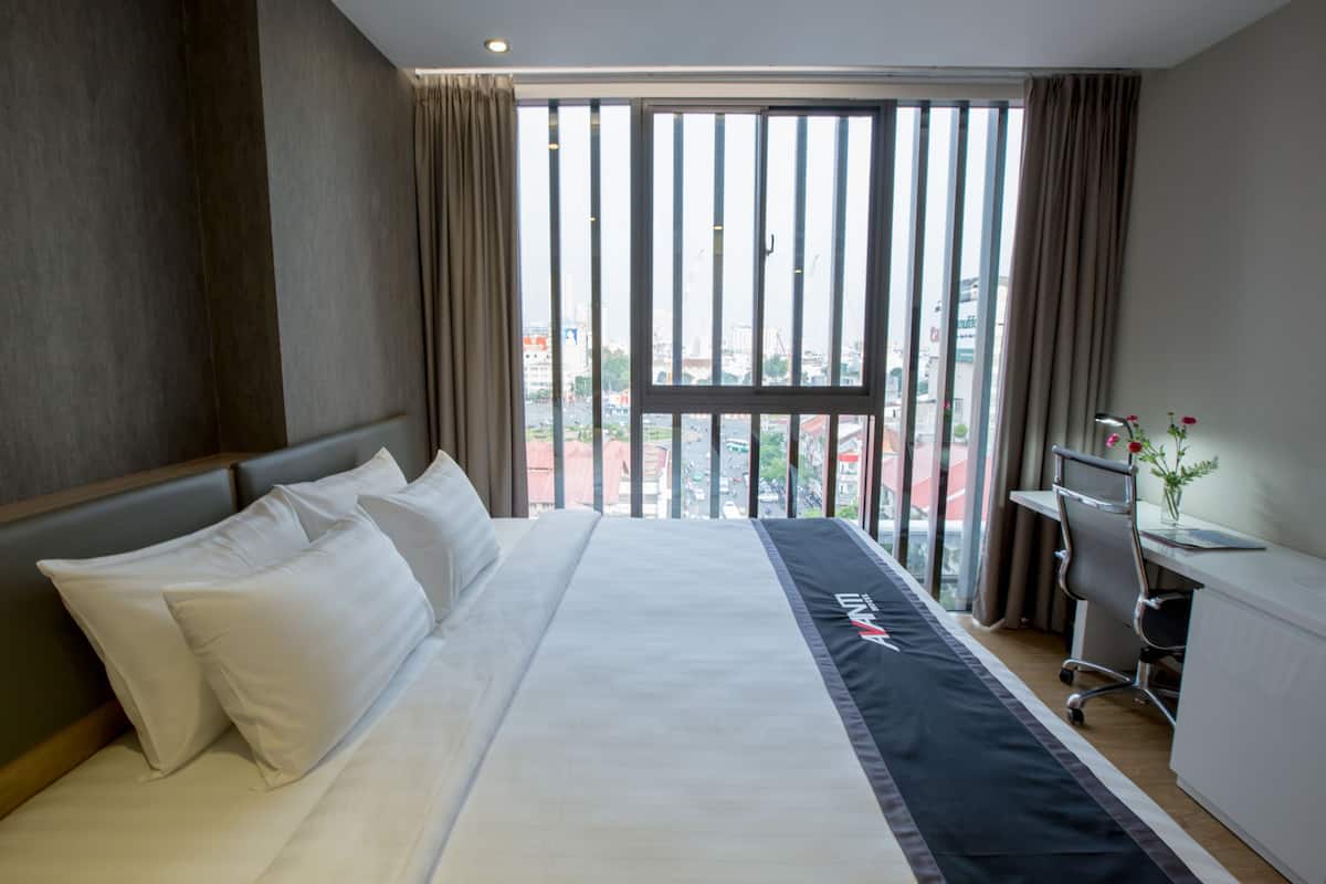 Ein Hotelzimmer mit einem großen Bett, einem Schreibtisch und Blick auf die Stadt durch das Fenster.