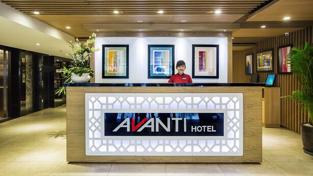 A reception desk at the Avanti Hotel with framed artwork on the wall and a potted plant to the side.