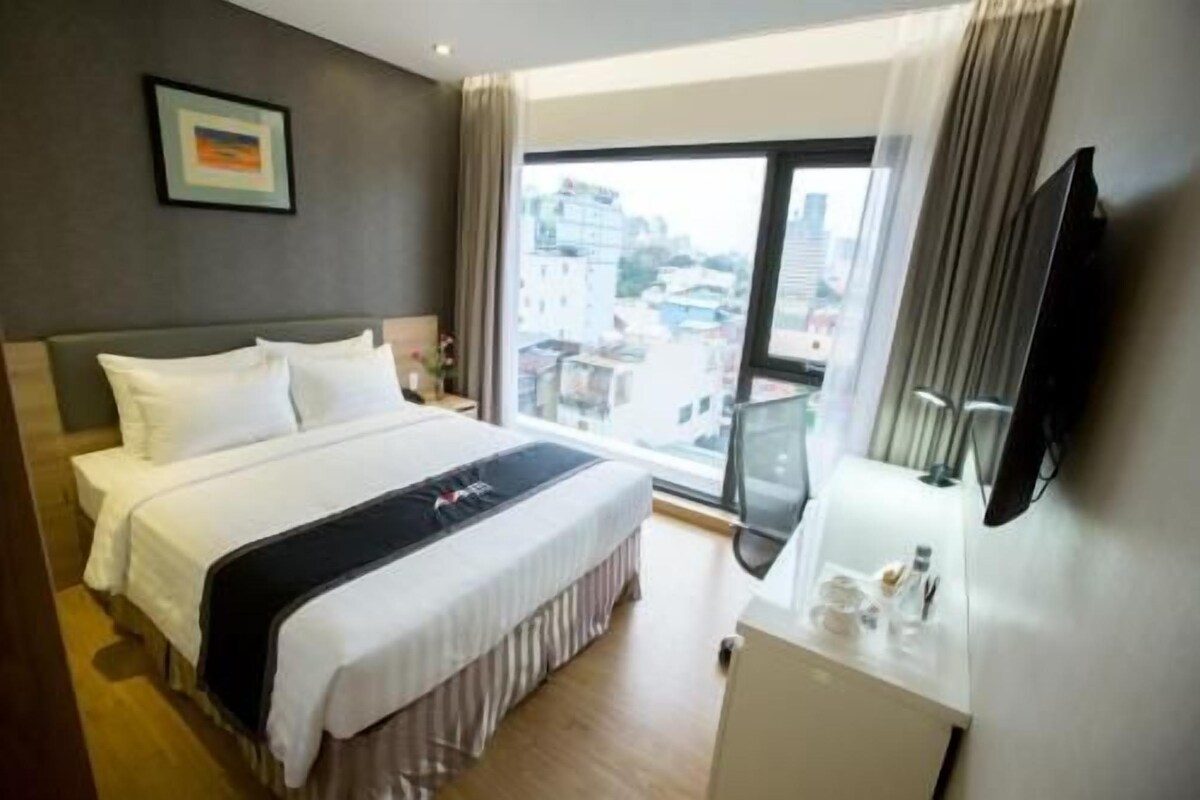 Habitación de hotel con cama, escritorio, televisor y ventana grande con vista a la ciudad.
