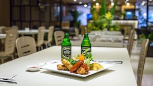 A dining table with a plate of food, two bottles of beer, and a small bowl of sauce.