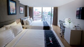 A hotel room with two beds, a desk, a TV, and a view of the city.