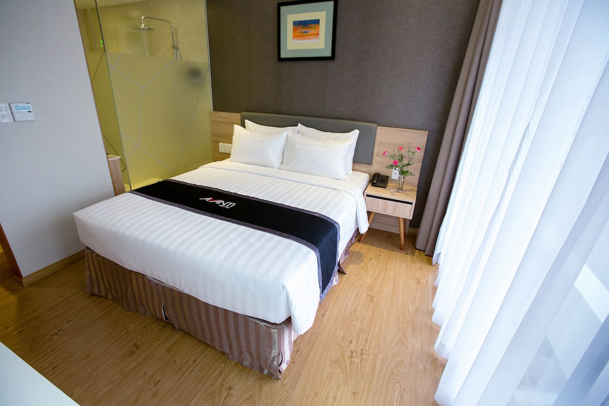 Ein Hotelzimmer mit einem großen Bett, einem Nachttisch mit Telefon und einem Duschbereich.