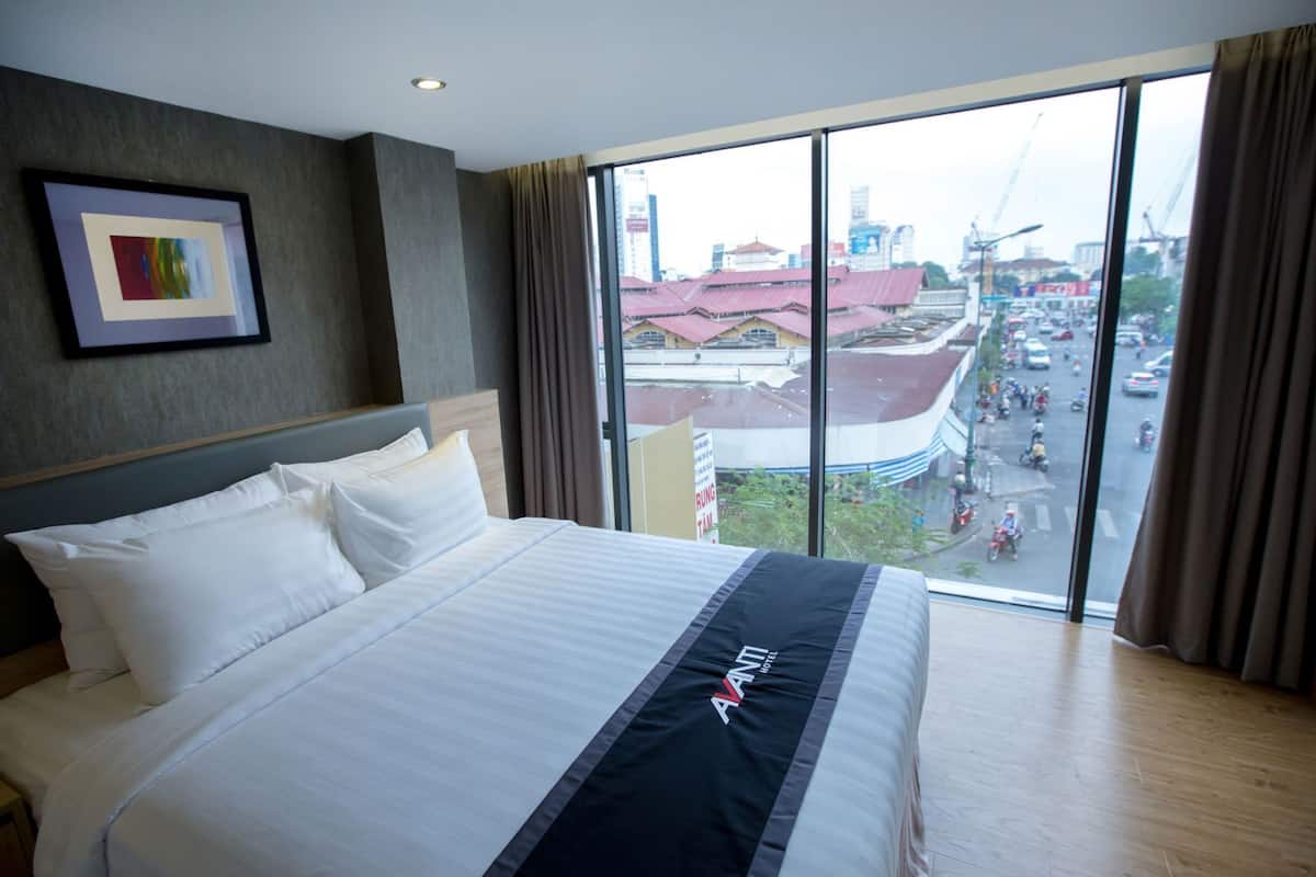 Ein Hotelzimmer mit einem großen Bett, einem gerahmten Bild an der Wand und Blick auf eine belebte Straße.