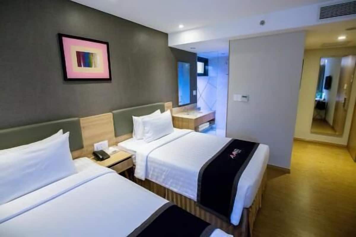 Ein Hotelzimmer mit zwei Betten, einem Nachttisch mit Telefon, einem kleinen Schreibtisch mit Spiegel und einer Tür zu einem Badezimmer.