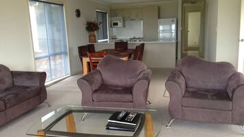 Una sala de estar moderna con una mesa de centro de vidrio, dos sofás morados y una zona de comedor con una mesa y sillas de madera.