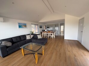 Una sala de estar moderna con un sofá modular, una mesa de centro de vidrio y un comedor con sillas y mesa de madera.
