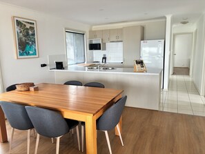 A modern kitchen with a wooden dining table and chairs, a microwave, and a refrigerator. - Kangaroo Island Bayview Villas (Kingscote)