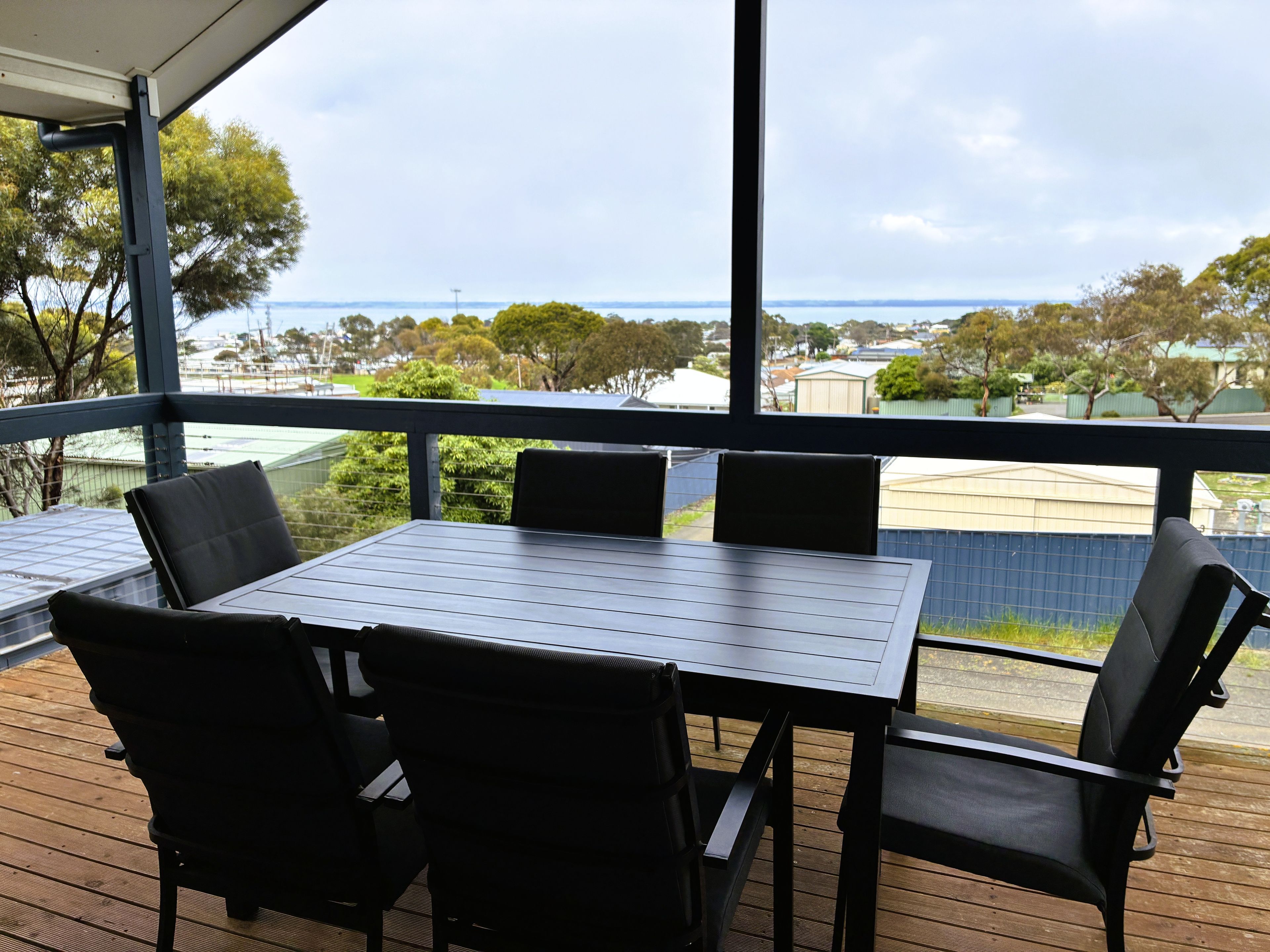 A covered outdoor area with a table and chairs, overlooking a residential area and a body of water.