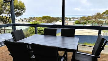 A covered outdoor area with a table and chairs, overlooking a residential area and a body of water.