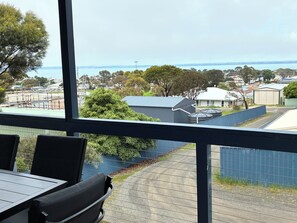 Blick vom Balkon mit Tisch und Stühlen auf ein Wohngebiet mit Häusern, Bäumen und einem Gewässer.