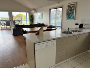 A modern kitchen with a dishwasher, a dining area with a table and chairs, and a view of the outdoors. - Kangaroo Island Bayview Villas (Kingscote)