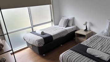 A modern bedroom with a bed, bedside tables, and a large window.