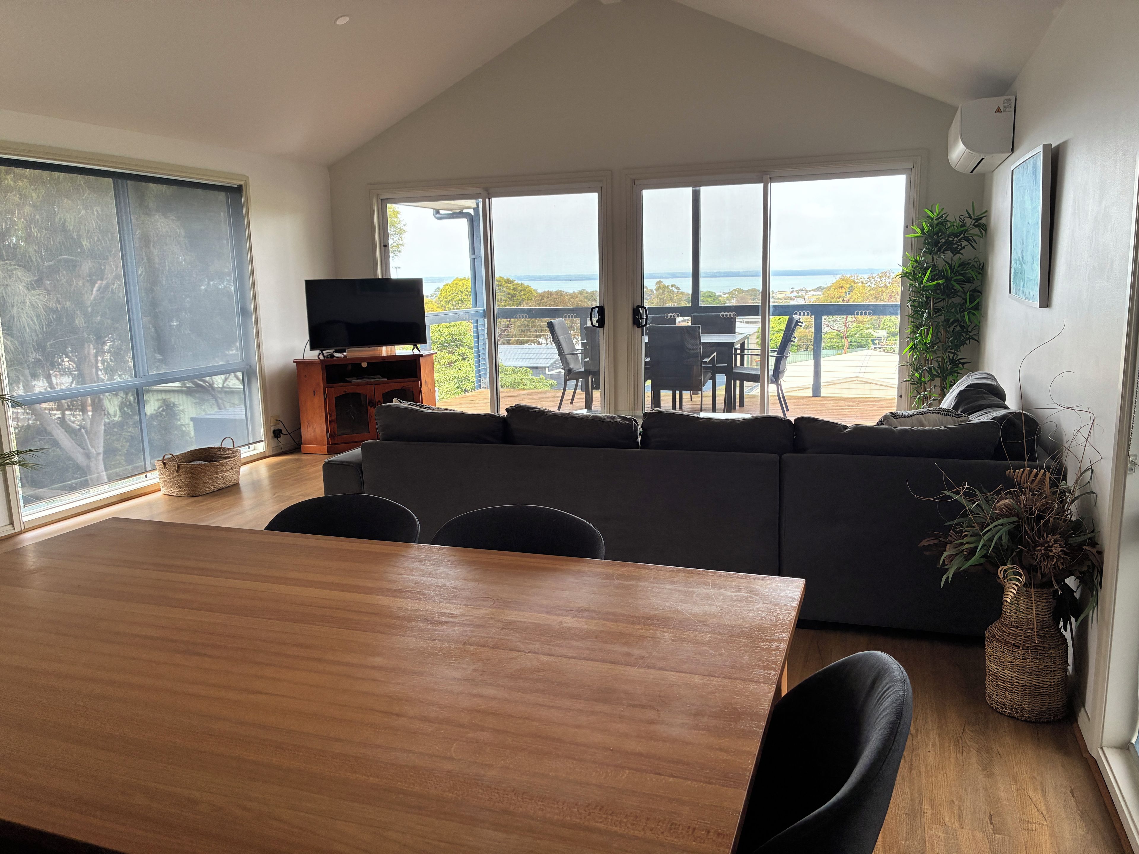 A modern living room with a large window, a wooden dining table, and a black sofa.