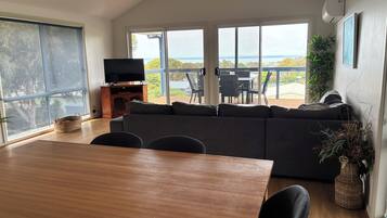 A modern living room with a large window, a wooden dining table, and a black sofa.