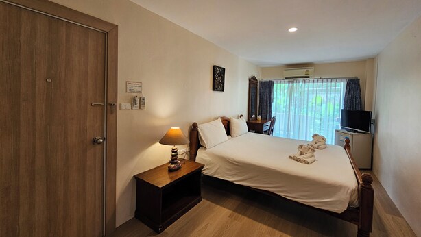 A hotel room with a wooden bed, a bedside table with a lamp, a TV, and a window with curtains. - Aonang Goodwill Hotel (Krabi)