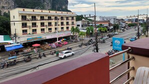 A multi-story building with balconies, a street with vehicles and pedestrians, and a mountainous backdrop. - Aonang Goodwill Hotel (Krabi)