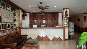 A reception area with a wooden bench, a small table, a fan, and a wall decorated with maps and pictures. - Aonang Goodwill Hotel (Krabi)