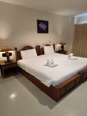 A neatly made bed with white linens and two rolled towels, wooden headboard, two bedside tables with lamps, and a framed picture on the wall. - Aonang Goodwill Hotel (Krabi)