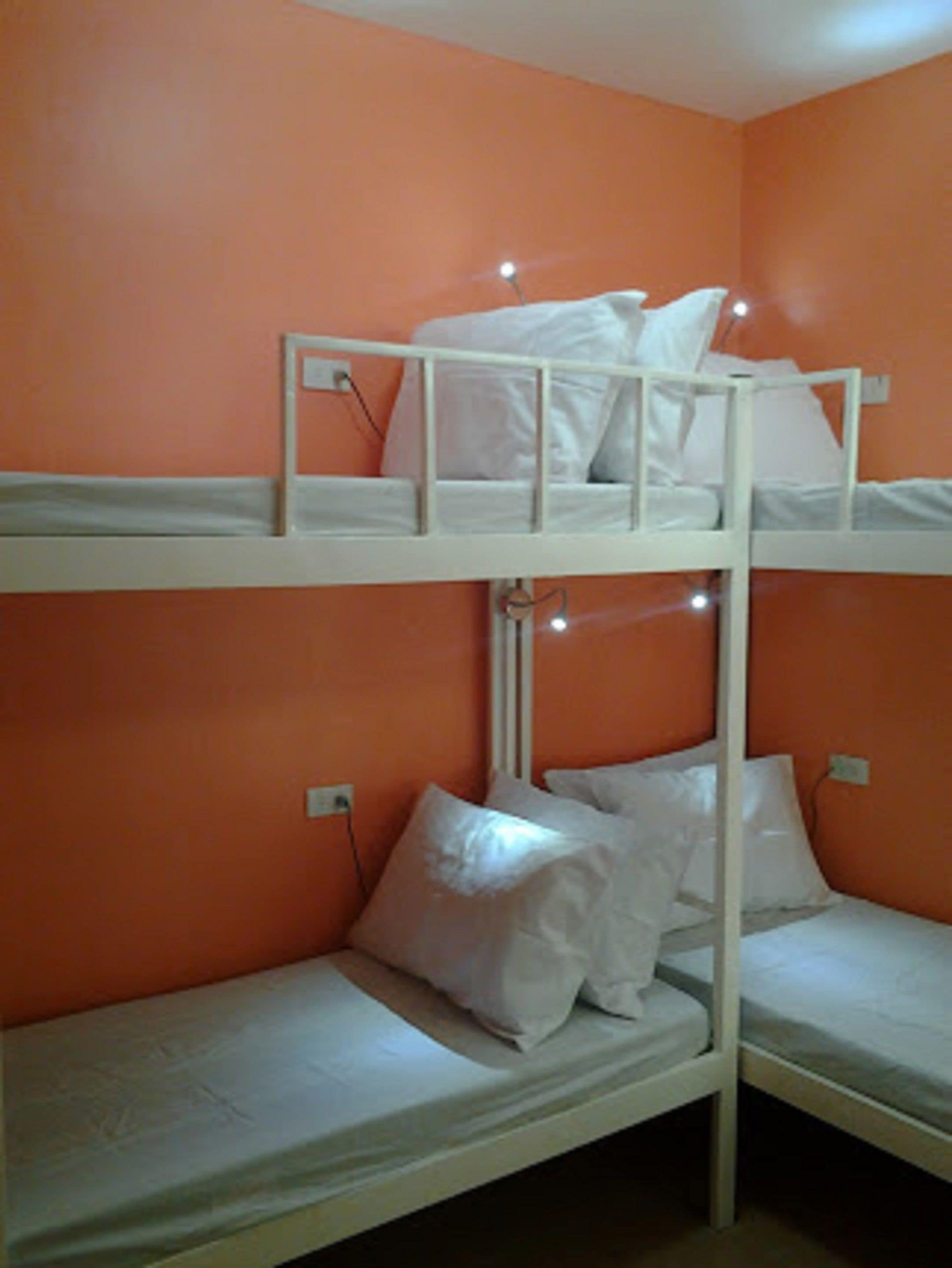 Dormitorio con literas, paredes anaranjadas y ropa de cama blanca.