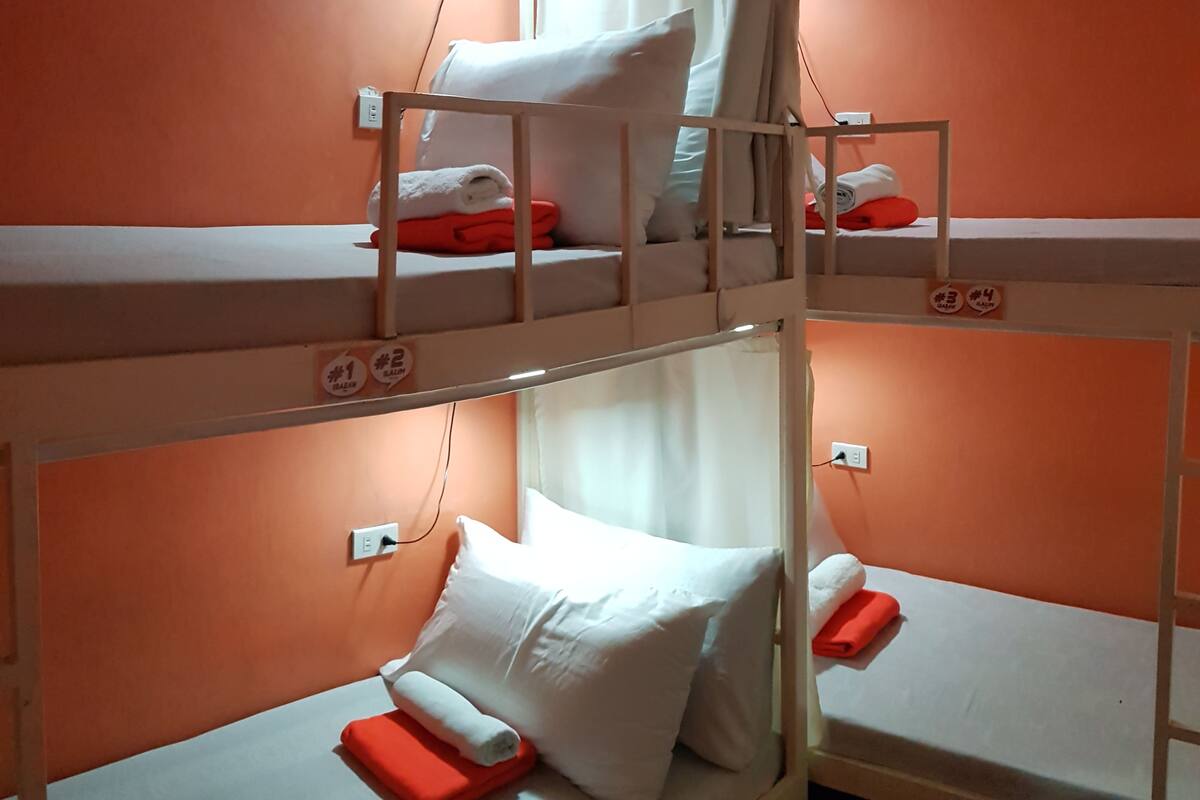 A bunk bed room with orange walls, white bedding, and a small window with curtains.
